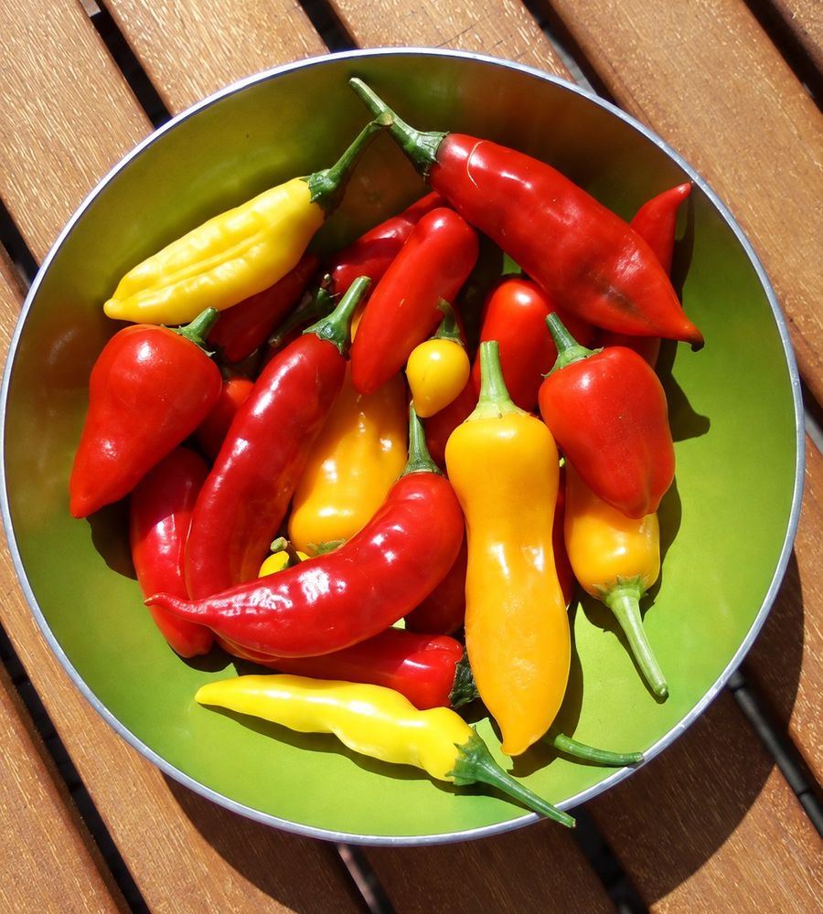 Rød og gul chili i en grønn bolle på et trebord